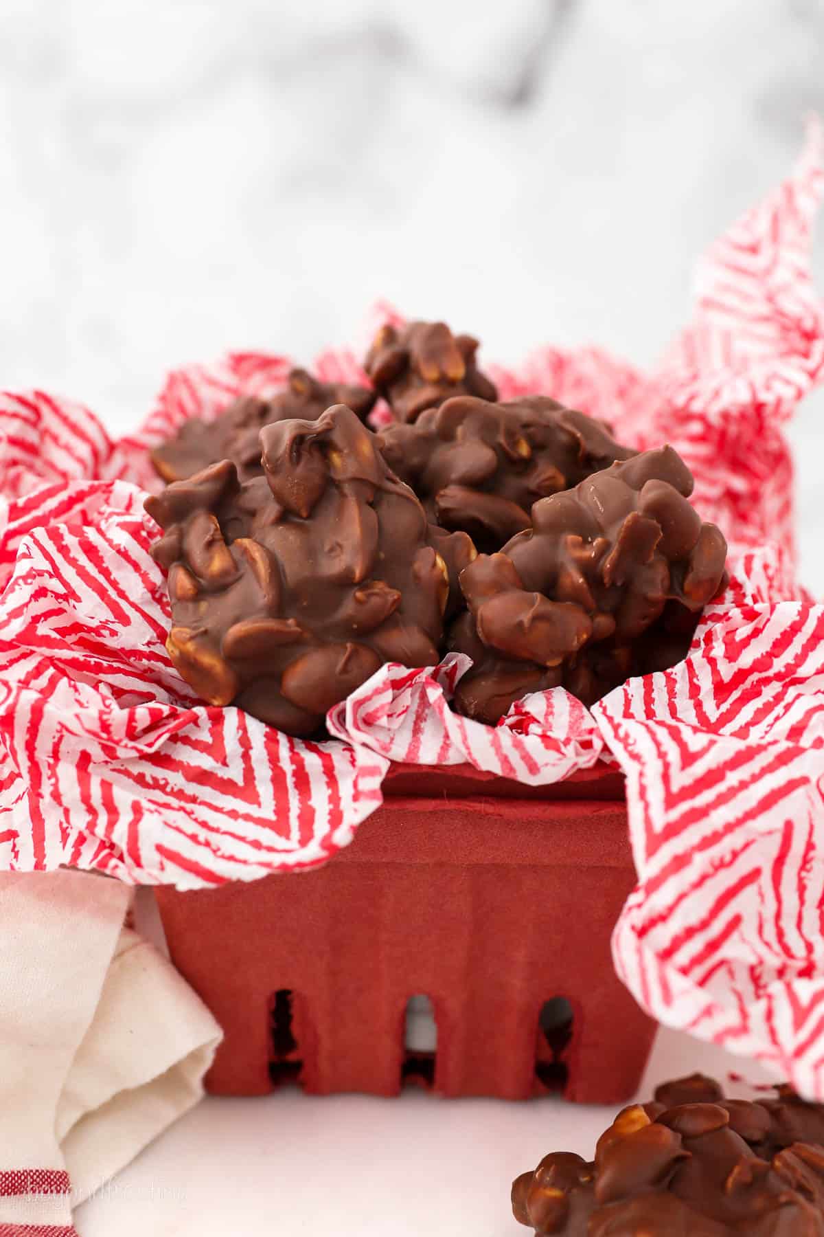 a red basket with tissue paper filled with homemade chocolate peanut clusters