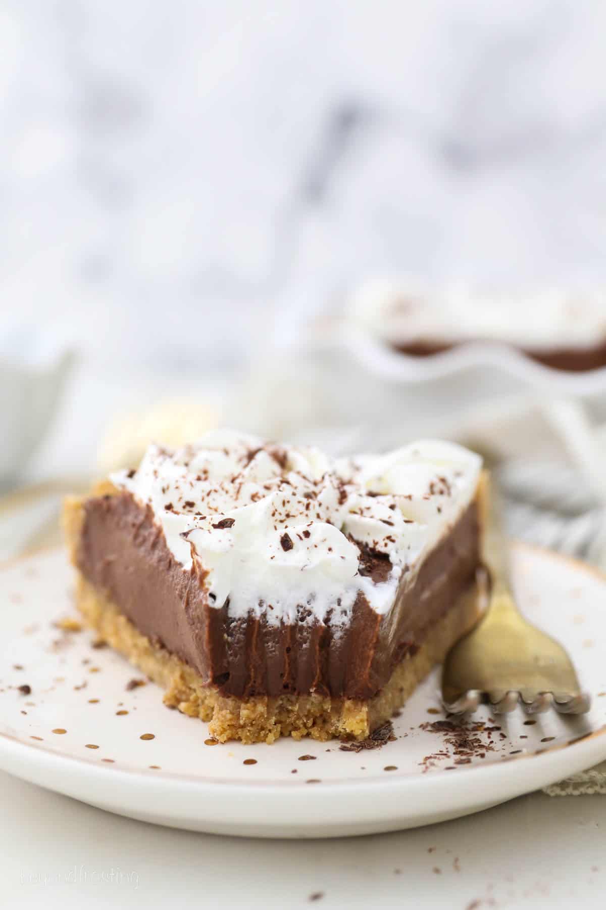 A slice of chocolate pudding pie on a polka dot plate with a bite missing and a gold fork next to it