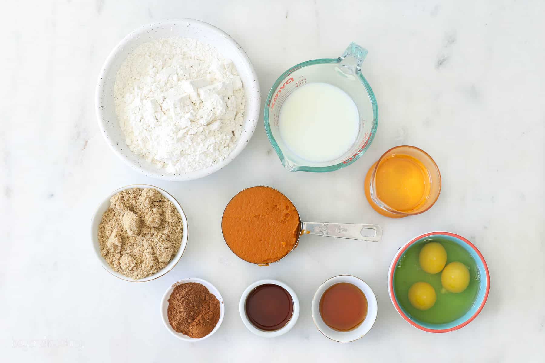 Ingredients for pumpkin cupcakes laid out in various bowls and measuring cups