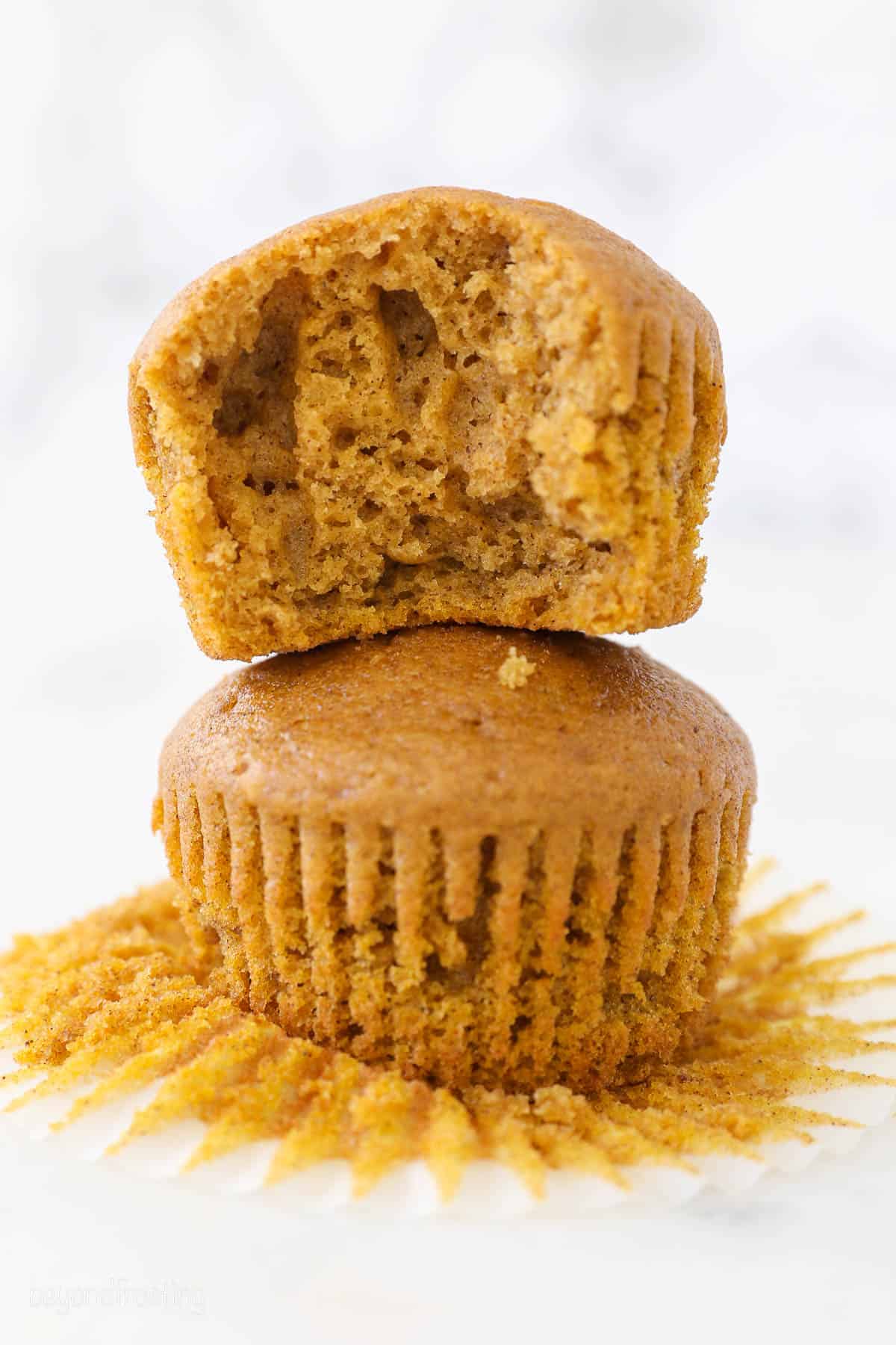 Two stacked unfrosted pumpkin cupcakes, the top one has a bite missing