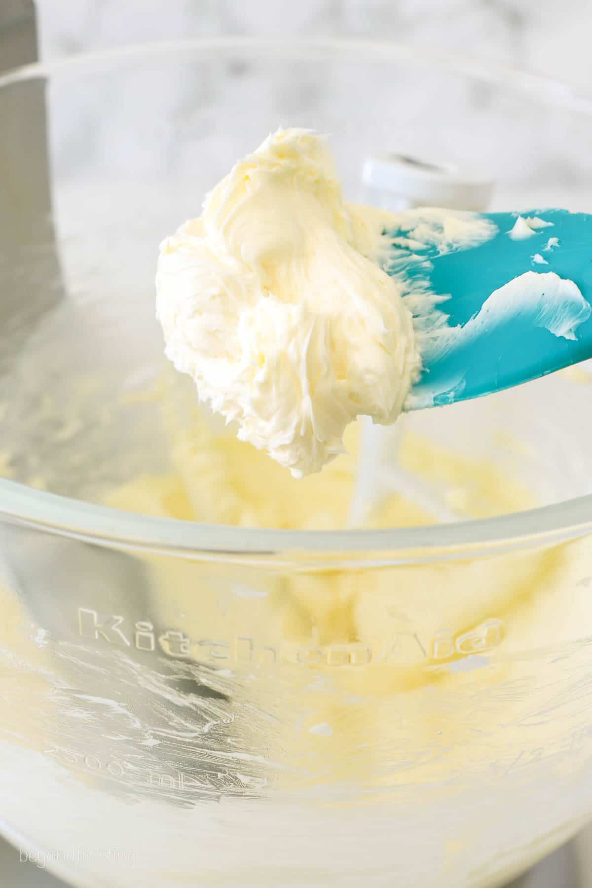 a teal spatula of whipped butter hanging over a mixing bowl with