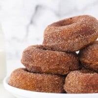 Pumpkin donuts piled high on a white plate.