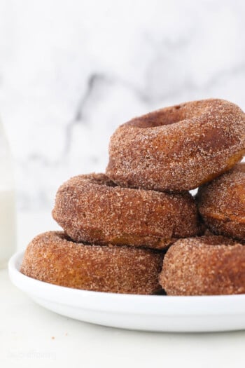 Pumpkin donuts piled high on a white plate.
