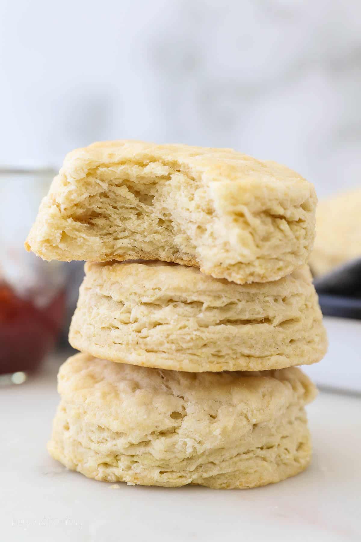 A stack of Buttermilk Biscuits with one bite taken out of the top biscuit. Biscuit layers are visible.