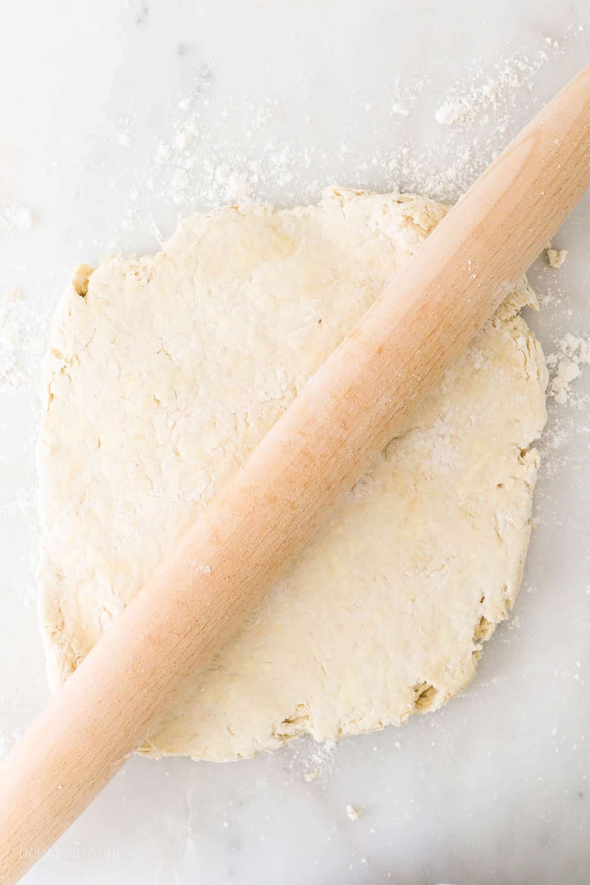Buttermilk Biscuit dough rolled out with wooden rolling pin resting on top of the dough.