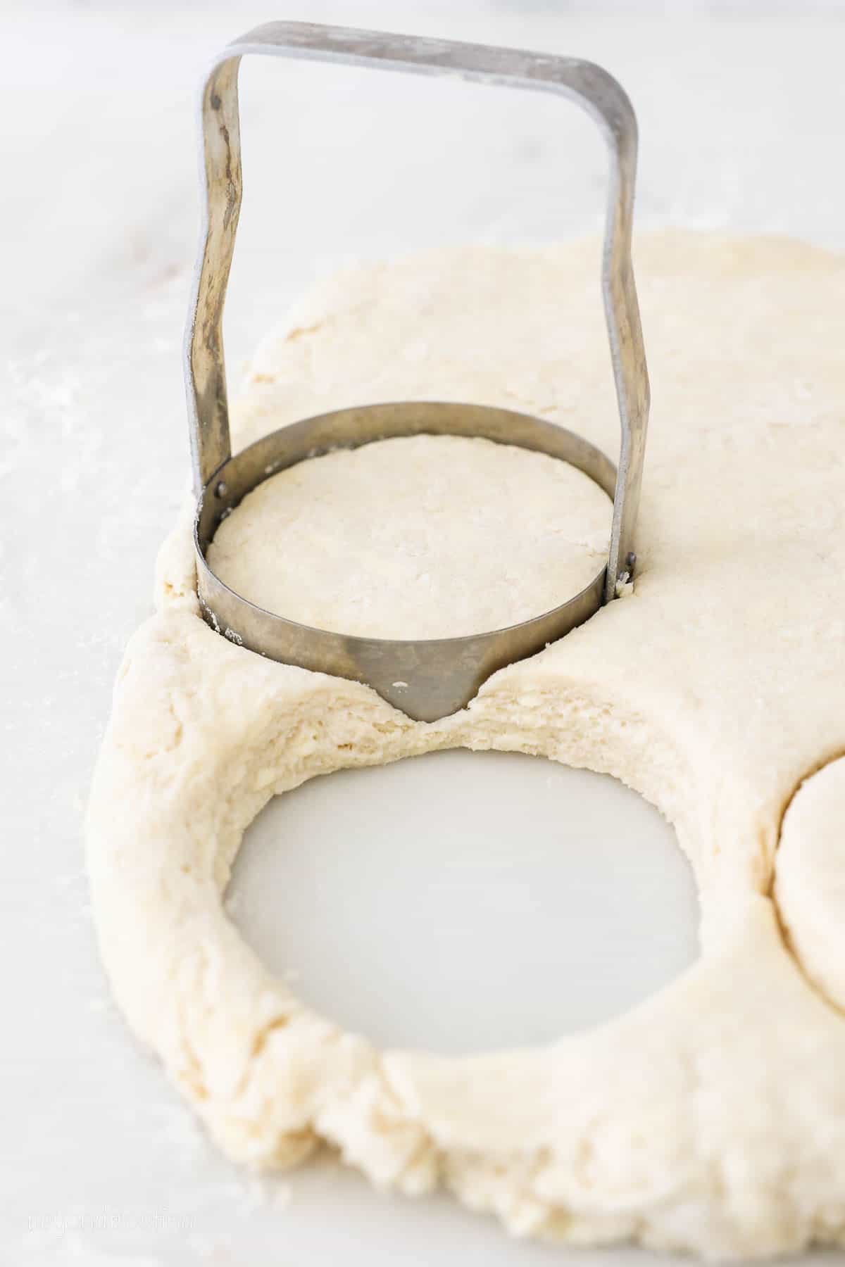 Round metal biscuit cutter cuts Buttermilk Biscuit shapes out of dough.