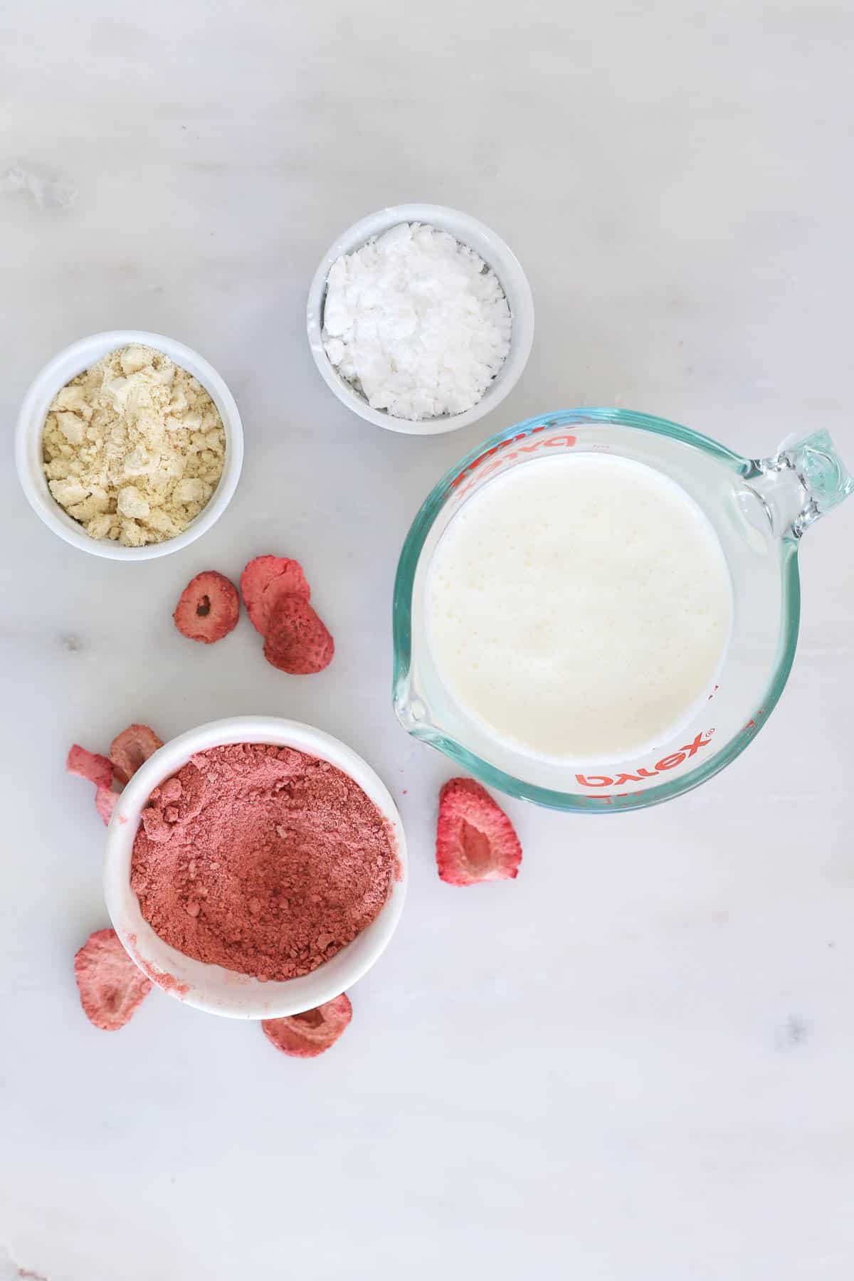 Ingredients for strawberry whipped cream in bowls: heavy cream, powdered strawberries, malt powder and powered sugar
