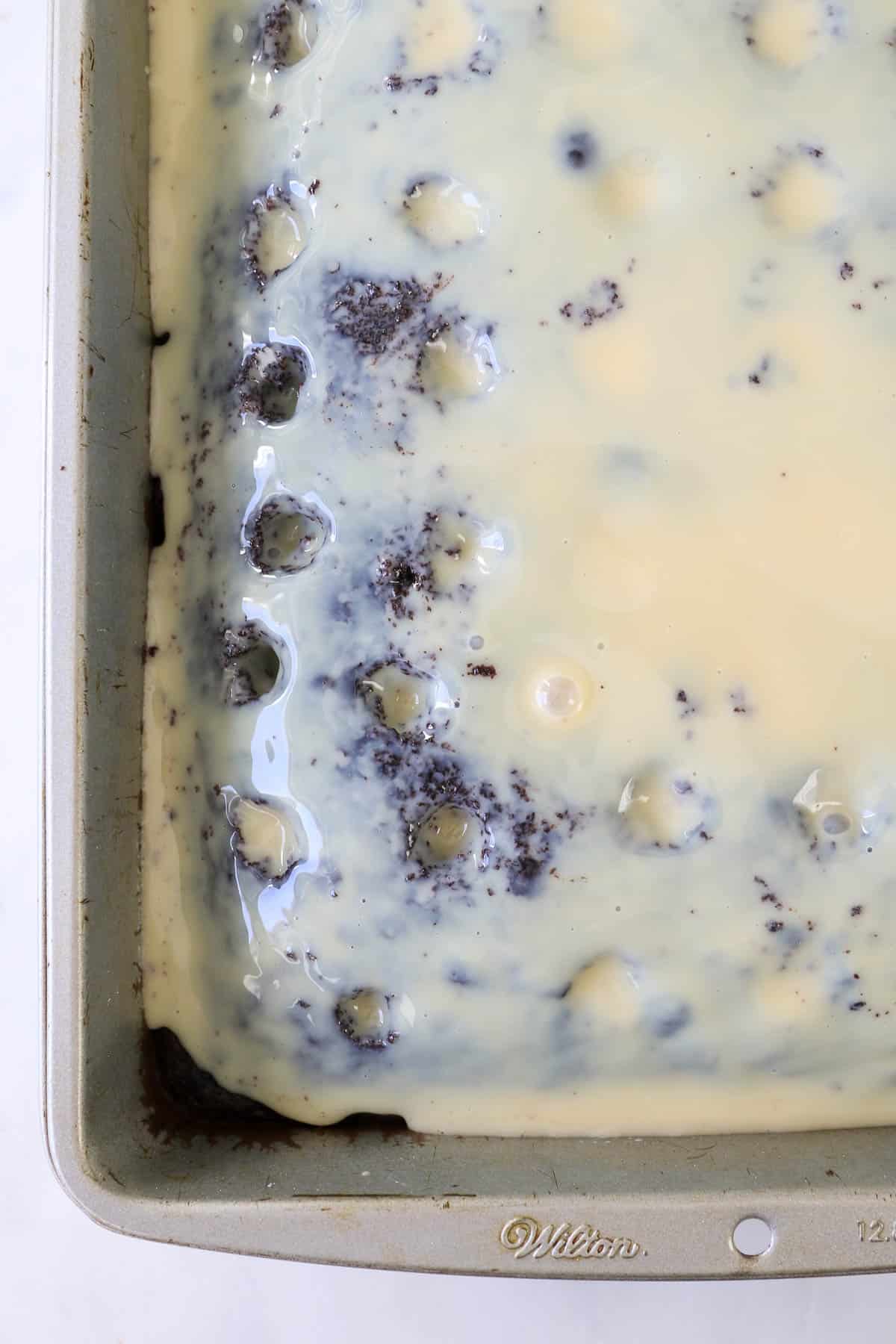 A close up of a chocolate cake with holes poked in it and sweetened condensed milk over top