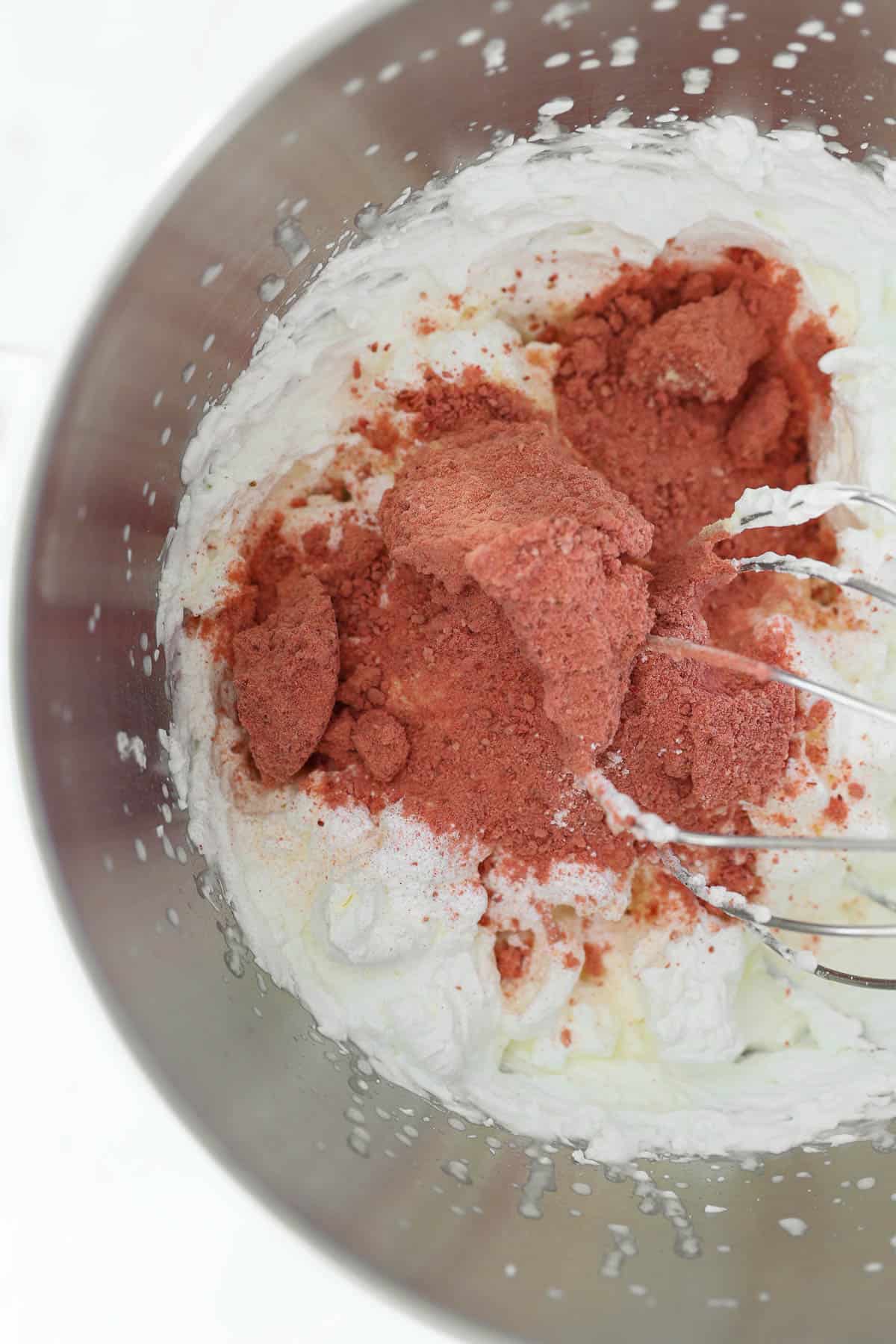 A metal kitchenaid mixing bowl with whipped cream and strawberry powder