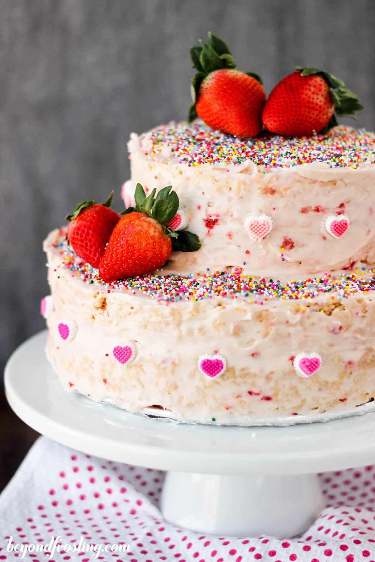 a strawberry rice krispie treat cake garnished with sprinkles and fresh strawberries on a cake stand