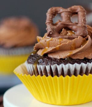 closeup of a take 5 cupcake topped with a chocolate covered pretzel in a yellow cupcake wrapper