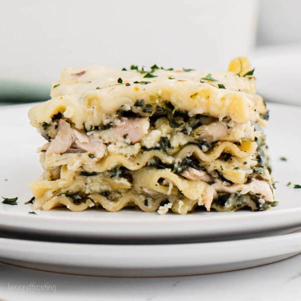 layered chicken and spinach lasagna on two stacked white plates