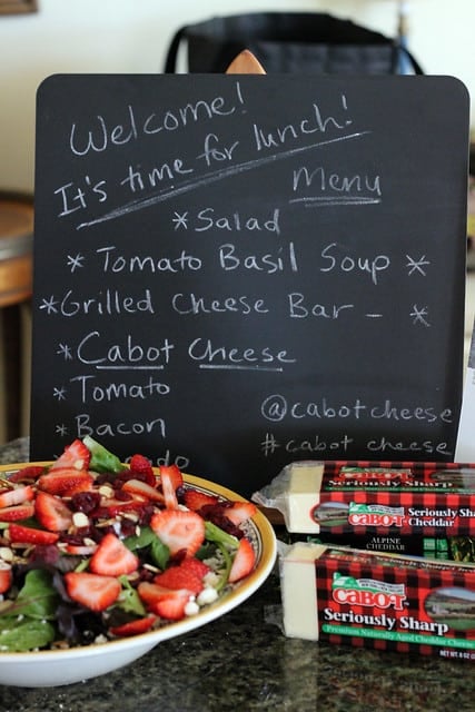 Lunch menu on a chalkboard sign with a salad and cheese in front