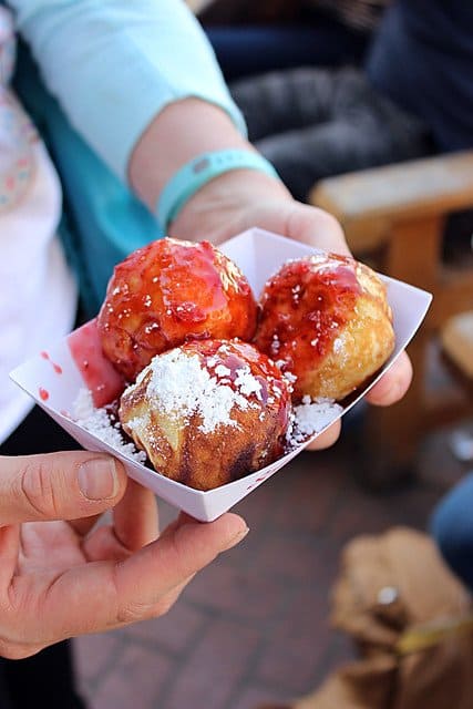 Three aebleskivers with berry sauce and powdered sugar in a paper dish