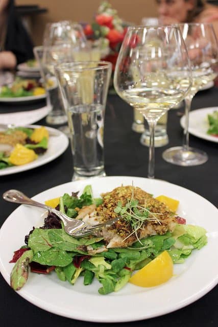 A plate of salad topped with fish on a table with glasses of wine