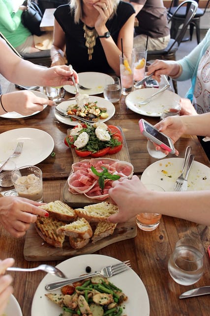 Three appetizers at the center of a dining table with people seated all around