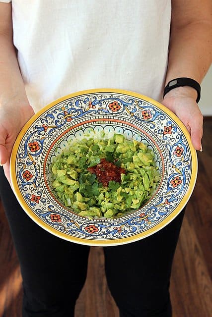 Hands holding a bowl of homemade guacamole