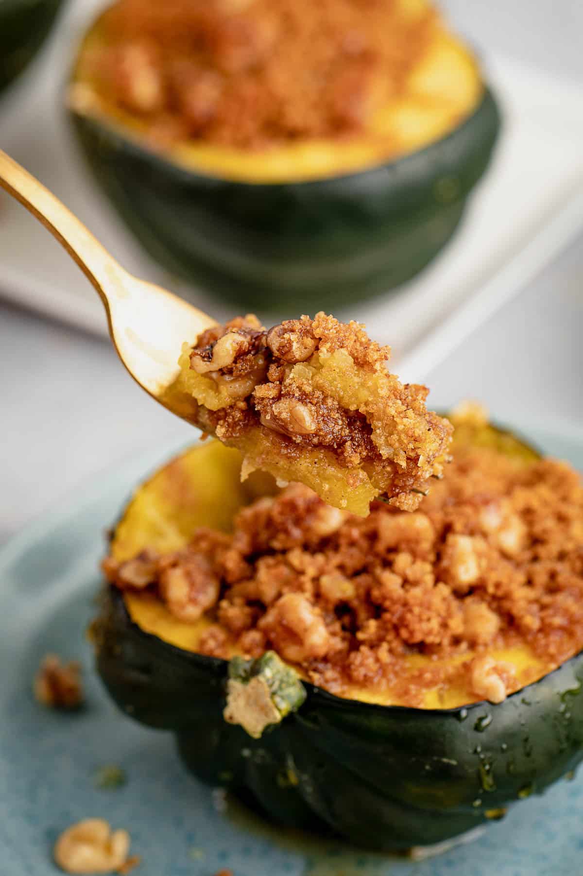 A forkful of baked acorn squash is lifted from one half of a stuffed acorn squash on a plate.