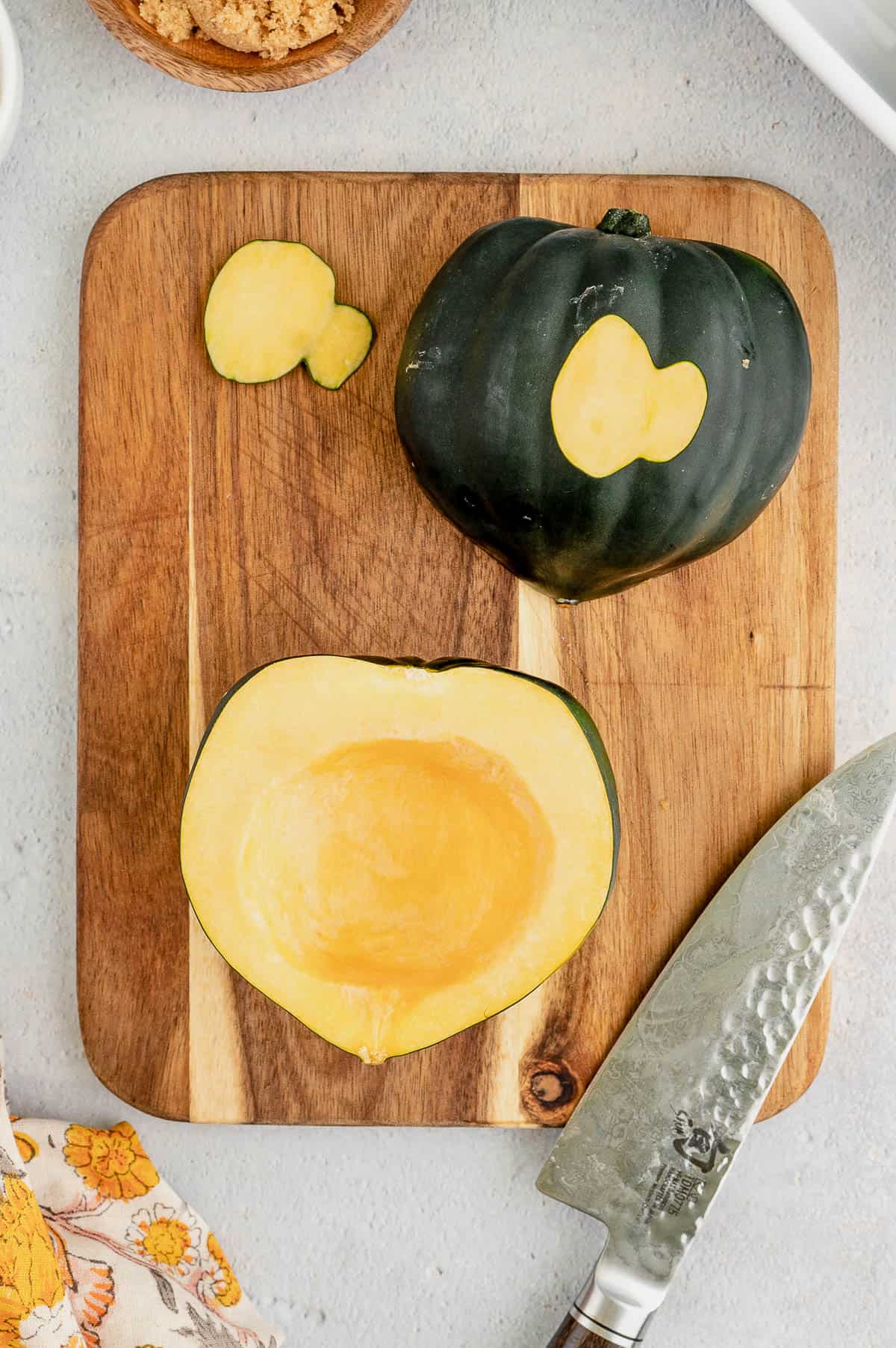 Acorn squash cut in half and seeded on a wooden cutting board, next to a knife.