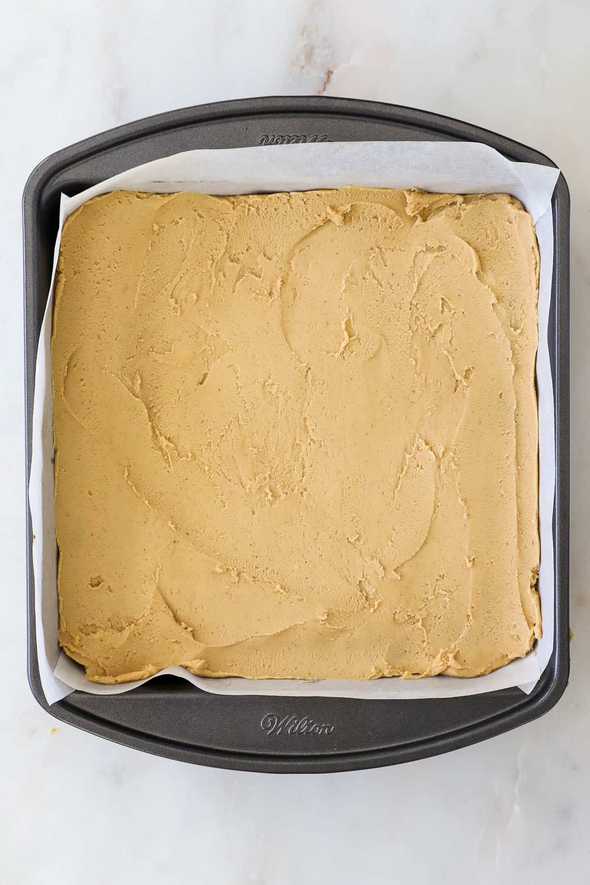 Overhead view of brownies in a parchment-lined pan topped with a peanut butter layer.