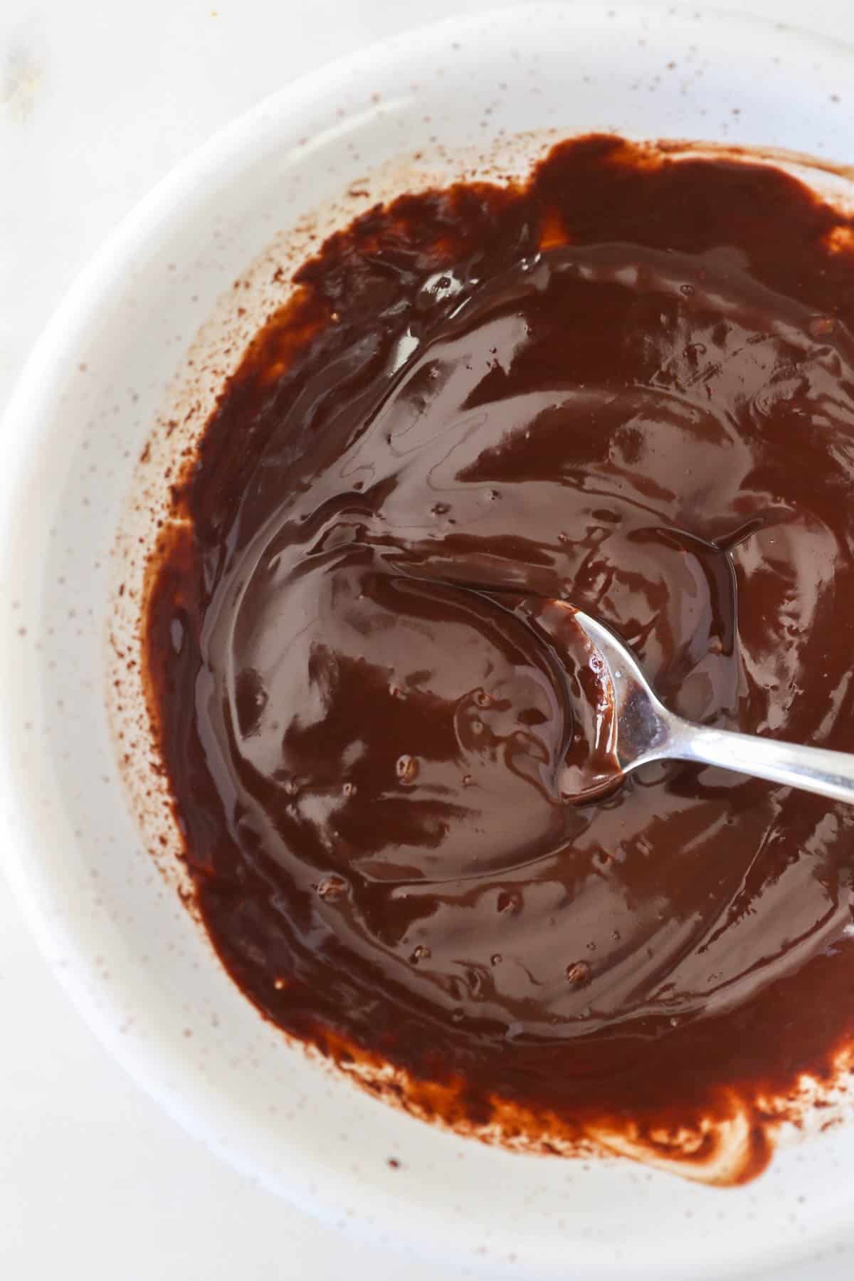 Melted chocolate ganache in a bowl with a spoon.