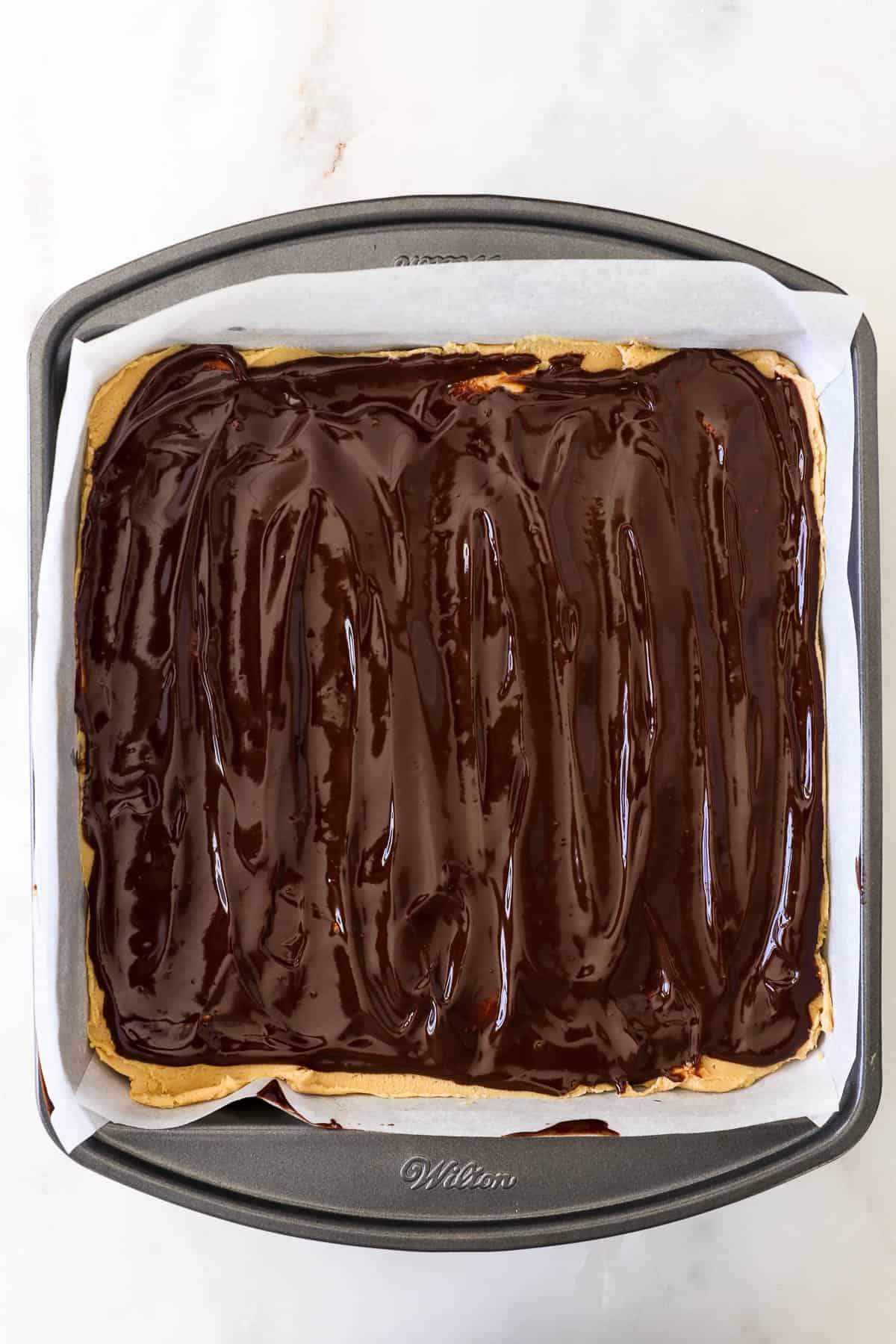 Overhead view of buckeye brownies in a parchment-lined pan topped with chocolate ganache.
