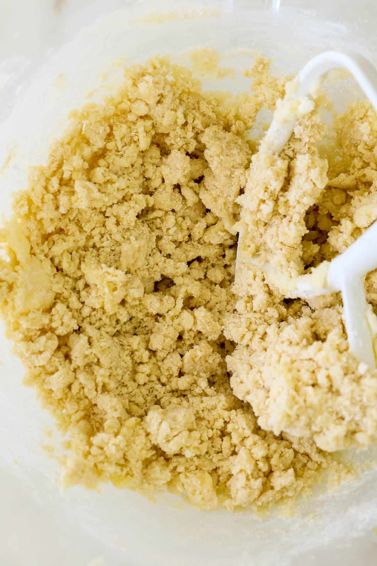 A crumbly cookie dough comes together in the bottom of a mixing bowl.