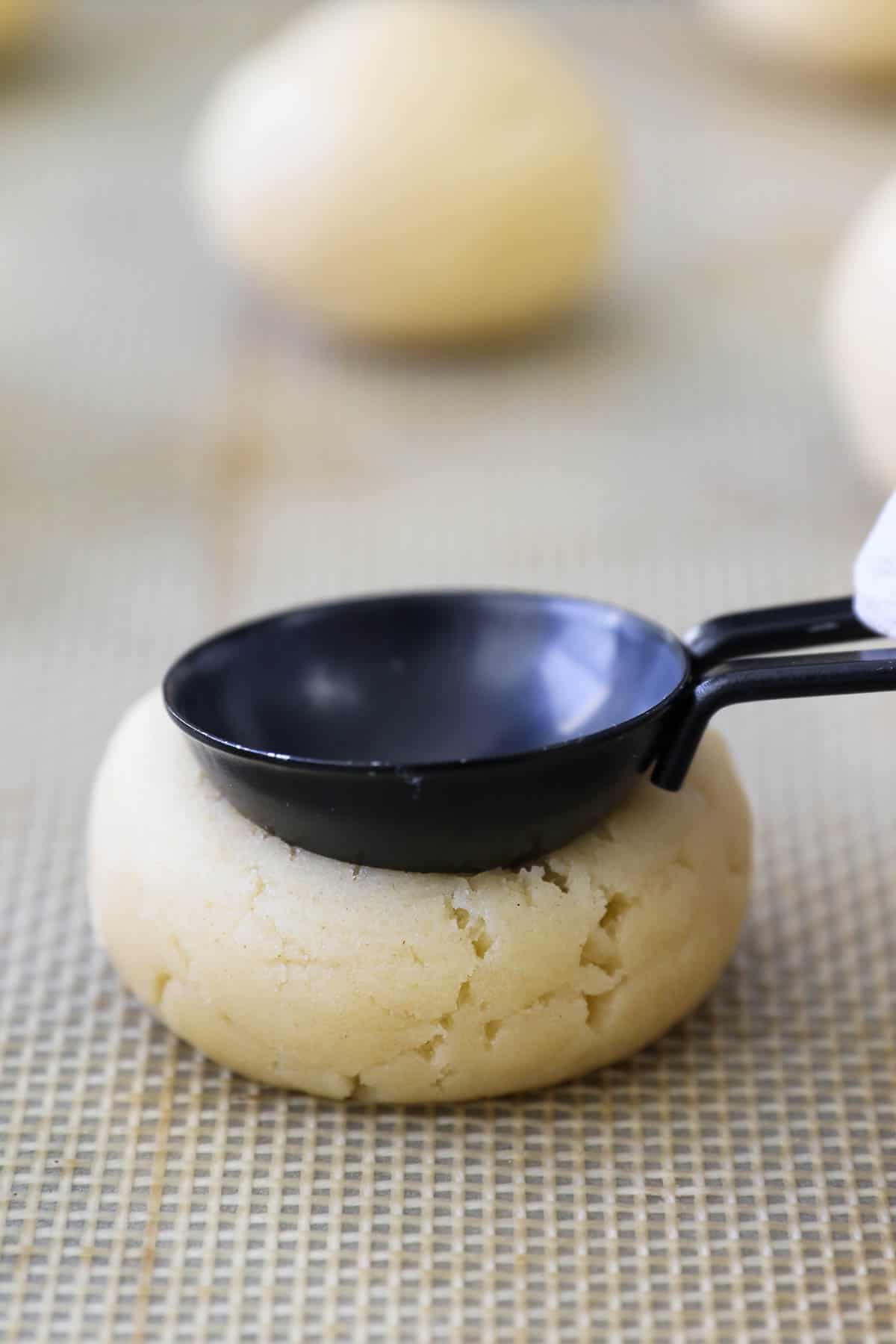 A teaspoon is used to press an indent into the top of a cookie dough ball.