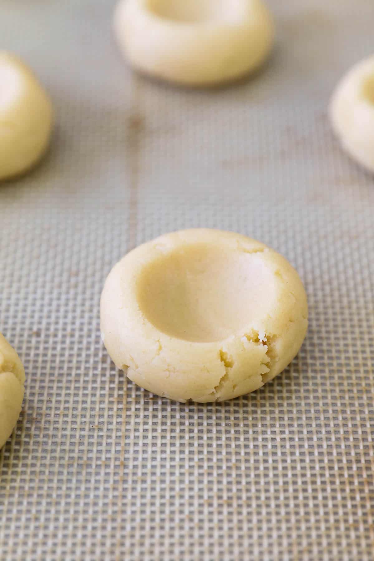Cookie dough balls with an indent in the top on a baking mat.