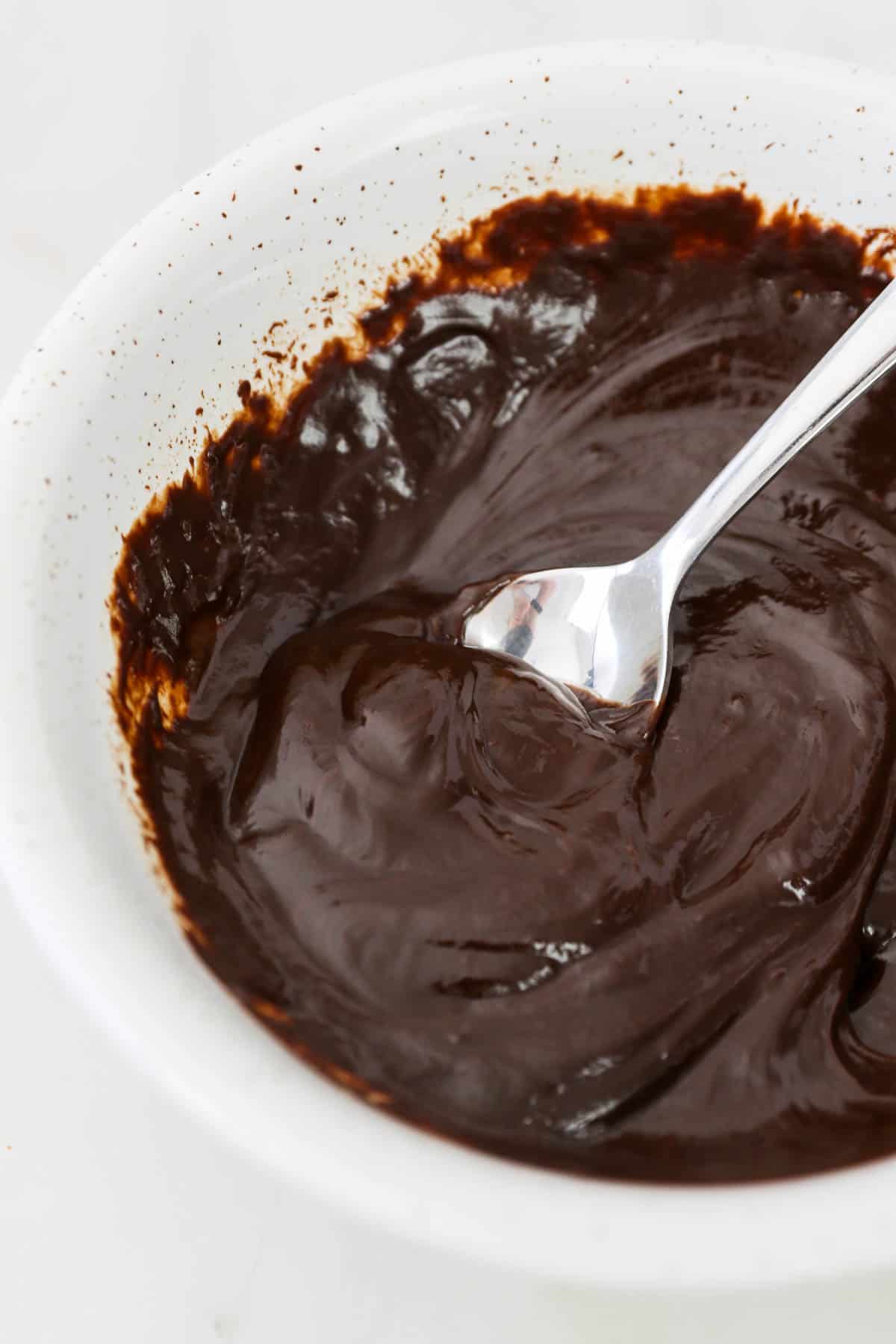 Chocolate ganache in a mixing bowl with a spoon.