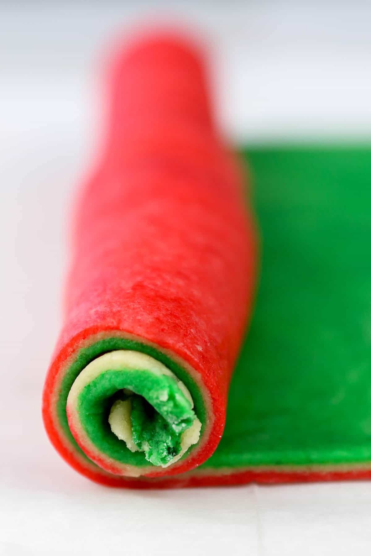 Layers of red, white, and green cookie dough is rolled up into a log.