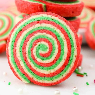 Close up of a Christmas pinwheel cookie with a stack of cookies behind it.