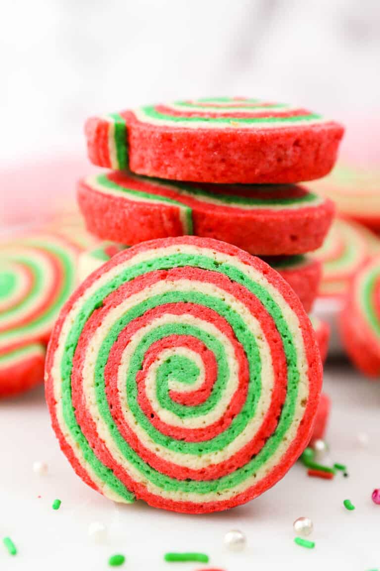 A Christmas pinwheel cookie with a stack of cookies behind it.