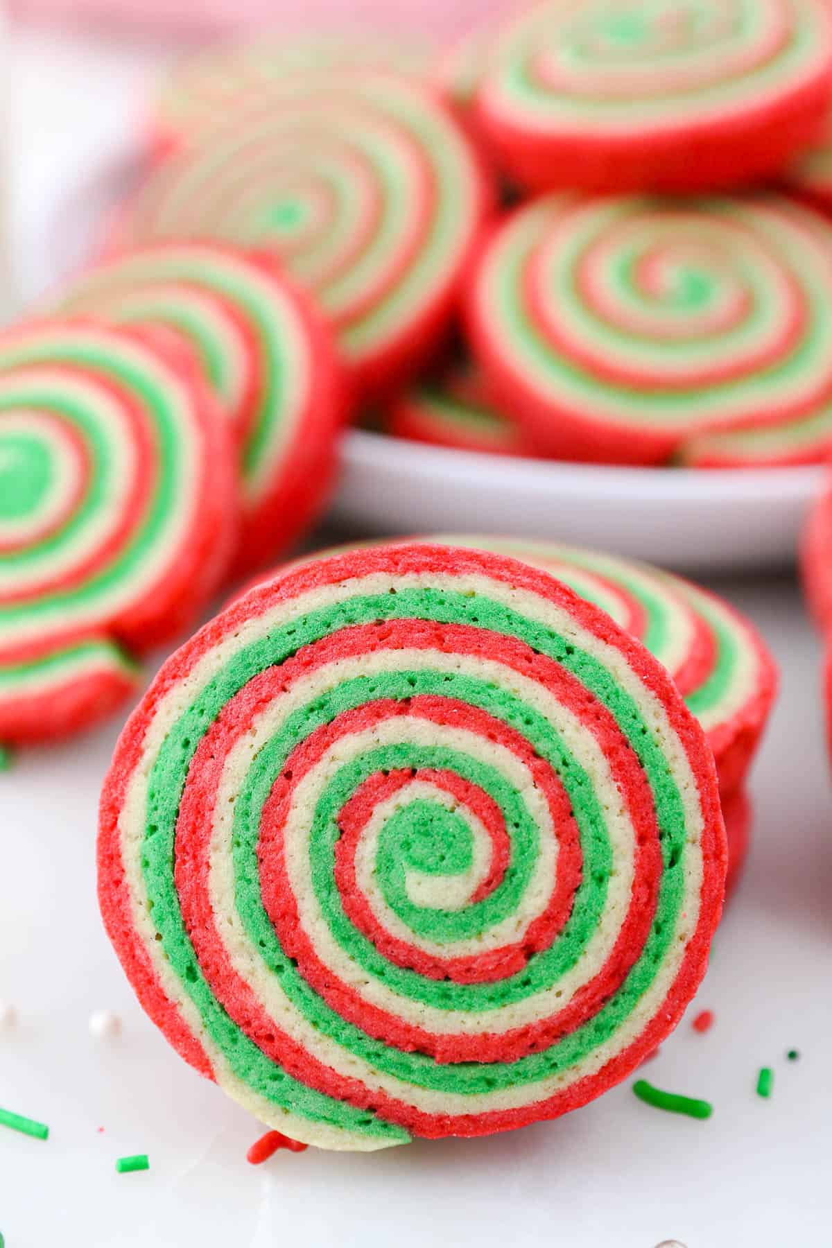 Christmas pinwheel cookies stacked and arranged around a white platter.