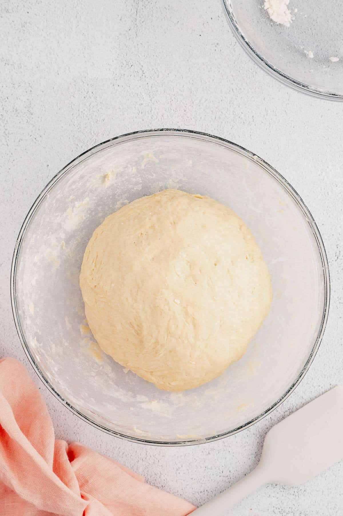 A ball of cinnamon roll dough in the bottom of a glass bowl.