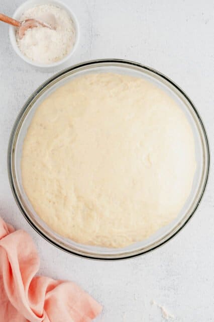 Risen cinnamon roll dough in a large glass bowl.