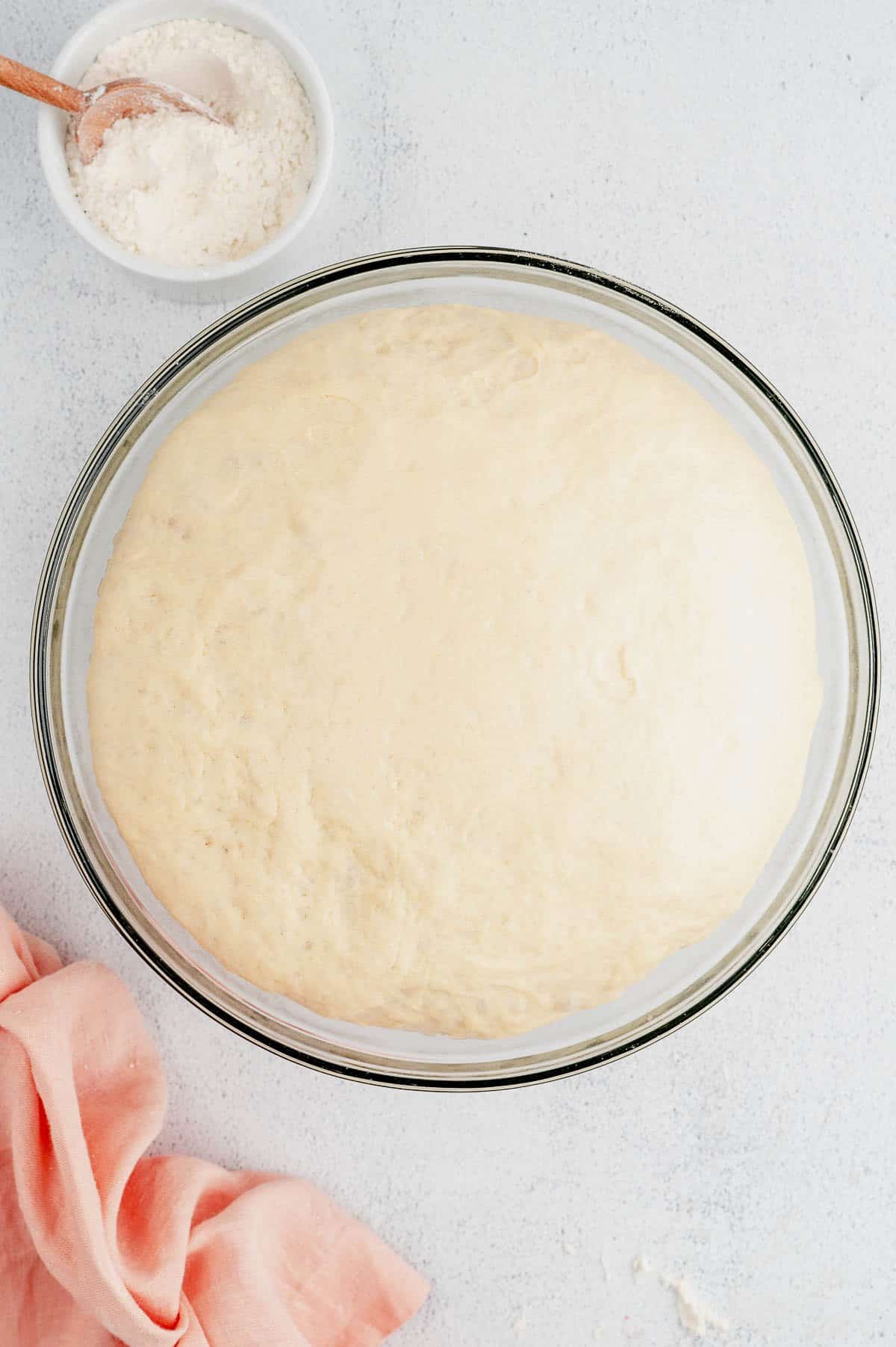 Risen cinnamon roll dough in a large glass bowl.