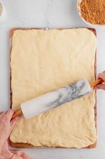 Two hands roll a rolling pin over a rectangle of dough.