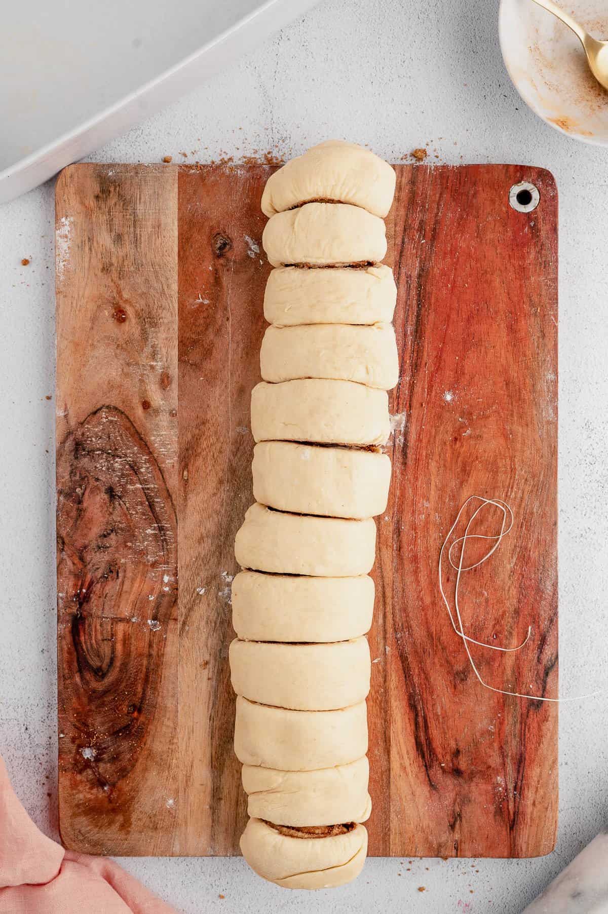 A dough log cut into cinnamon rolls on a wooden cutting board.