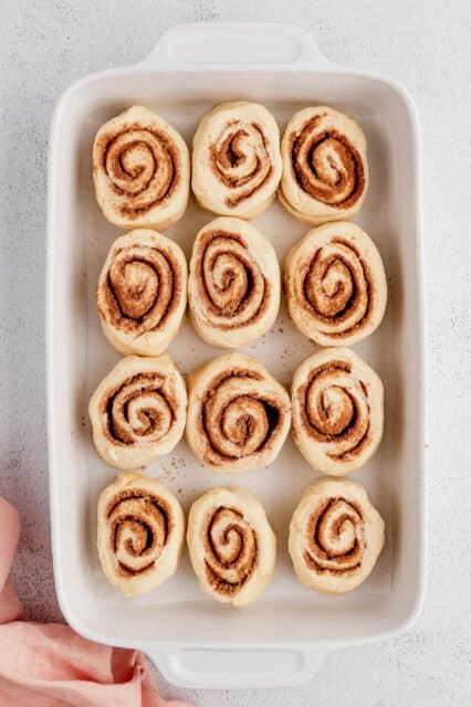 Unbaked cinnamon rolls inside a white ceramic baking dish.
