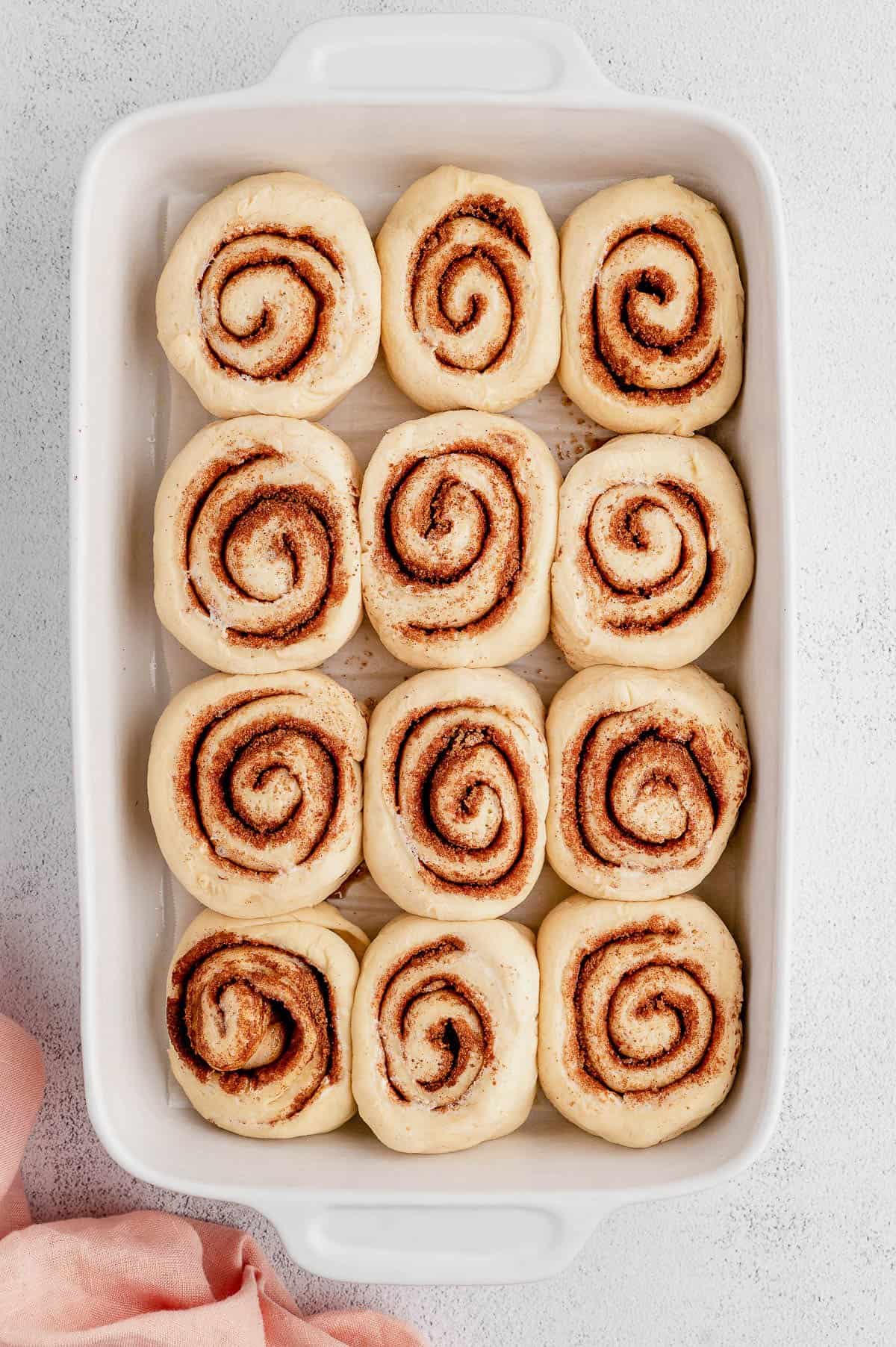 Risen unbaked cinnamon rolls inside a white ceramic baking dish.