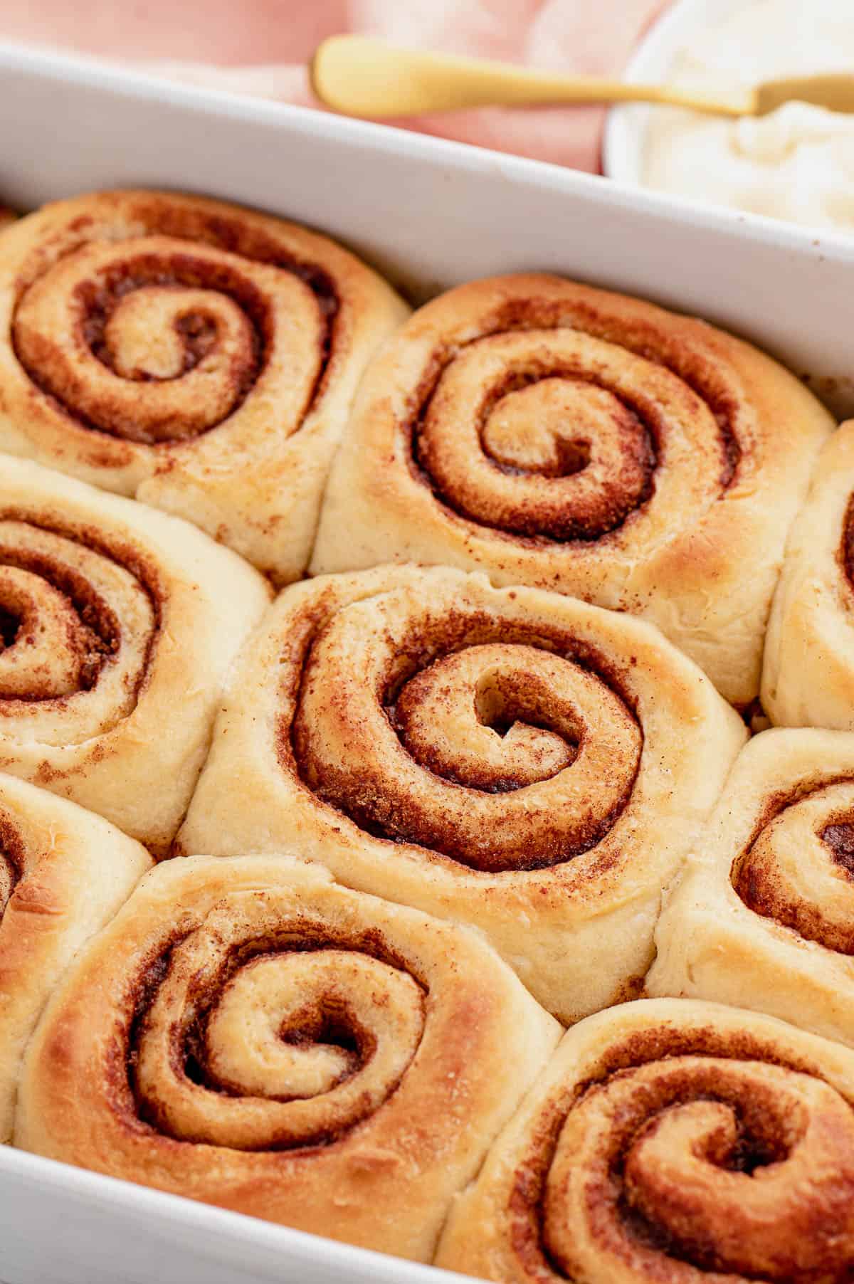 Baked, unfrosted overnight cinnamon rolls in a white baking dish.