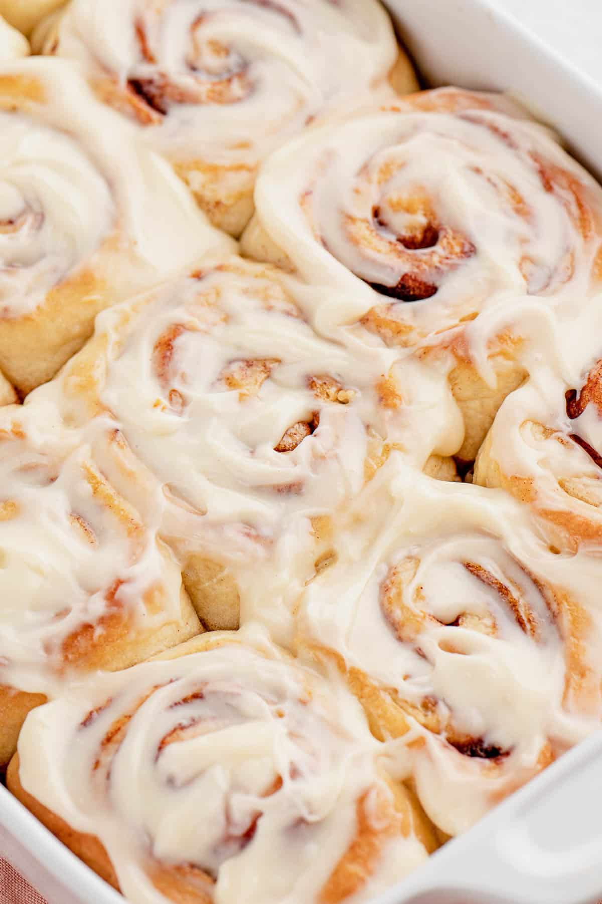 Frosted overnight cinnamon rolls in a white baking dish.