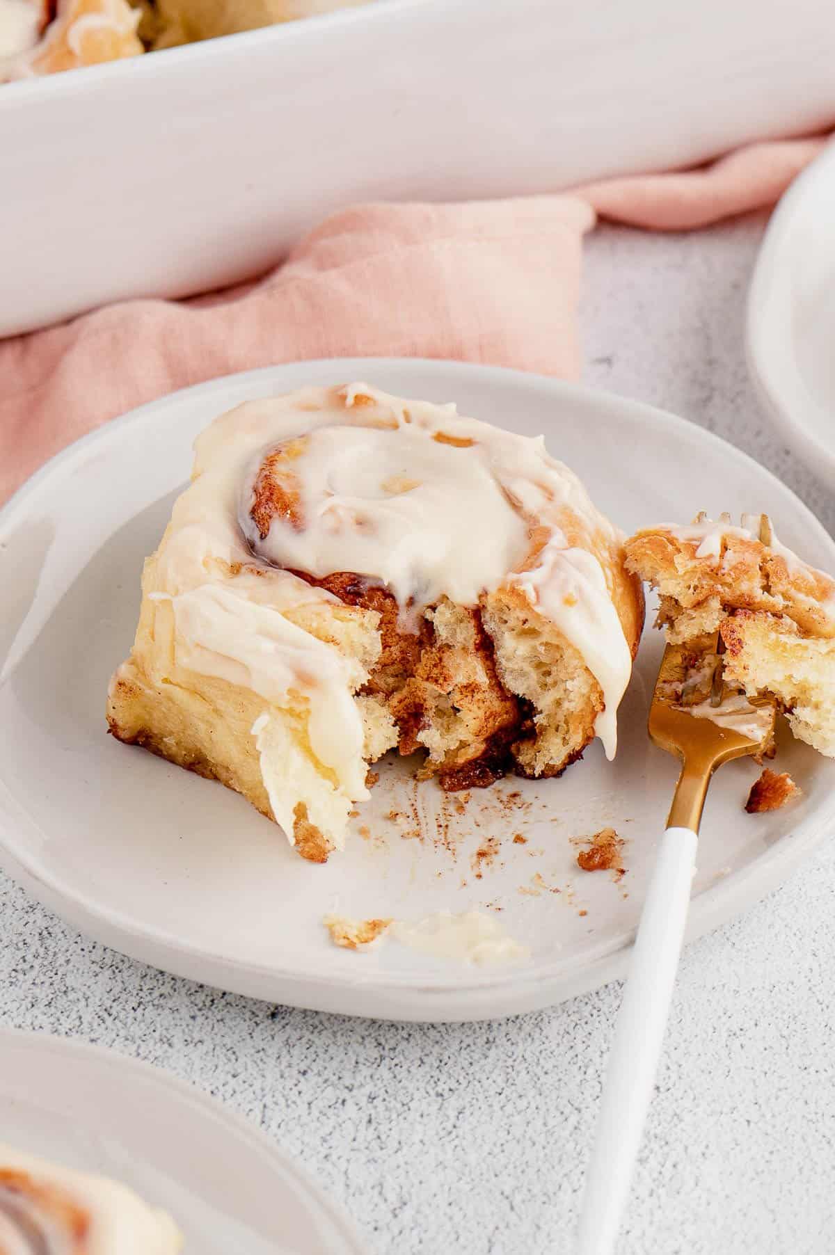 A frosted overnight cinnamon roll on a white plate with a forkful missing.