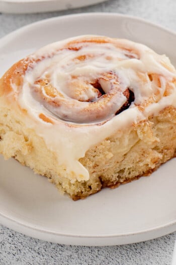 A frosted overnight cinnamon roll on a white plate next to a fork.