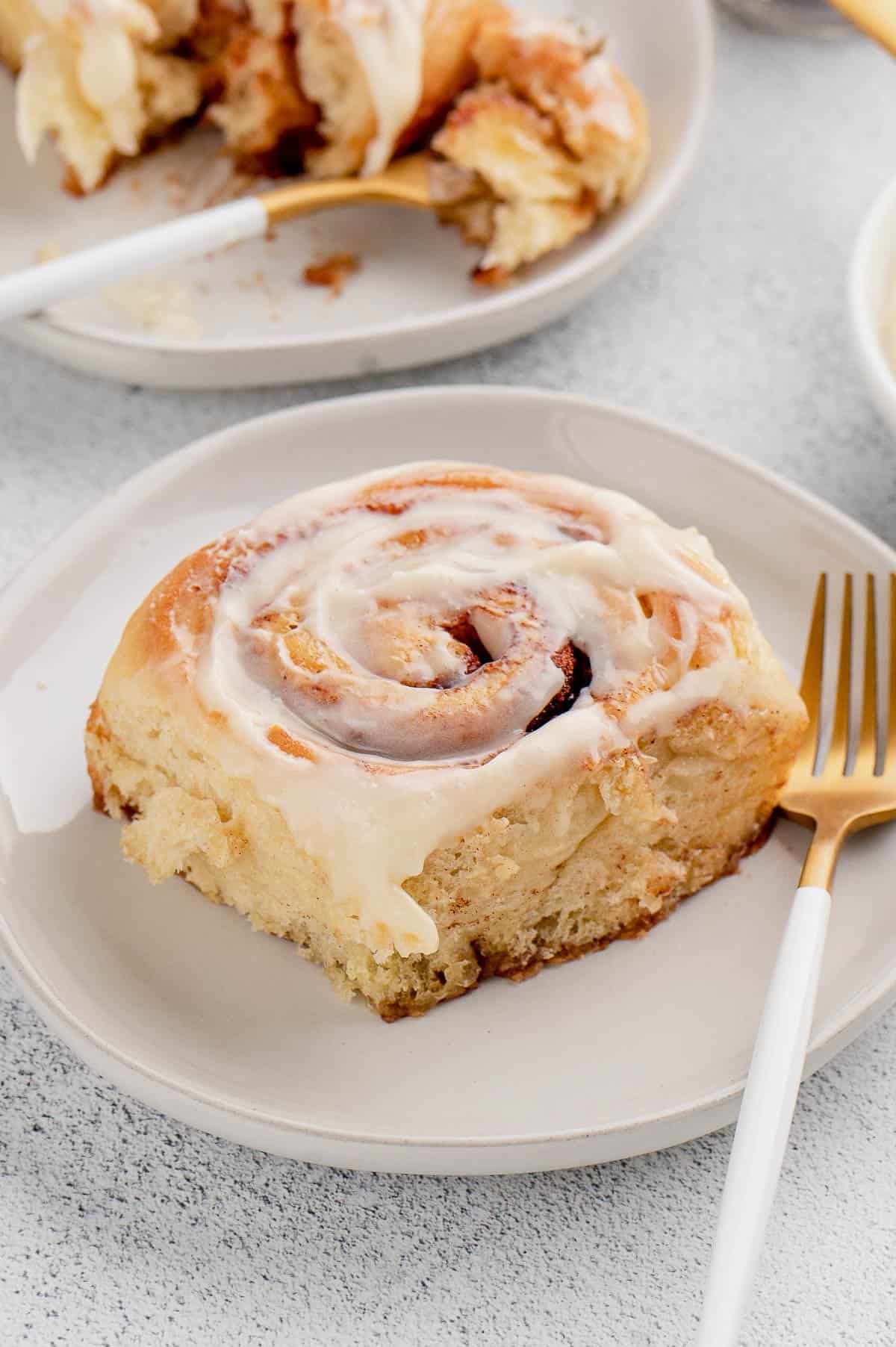 A frosted overnight cinnamon roll on a white plate next to a fork.