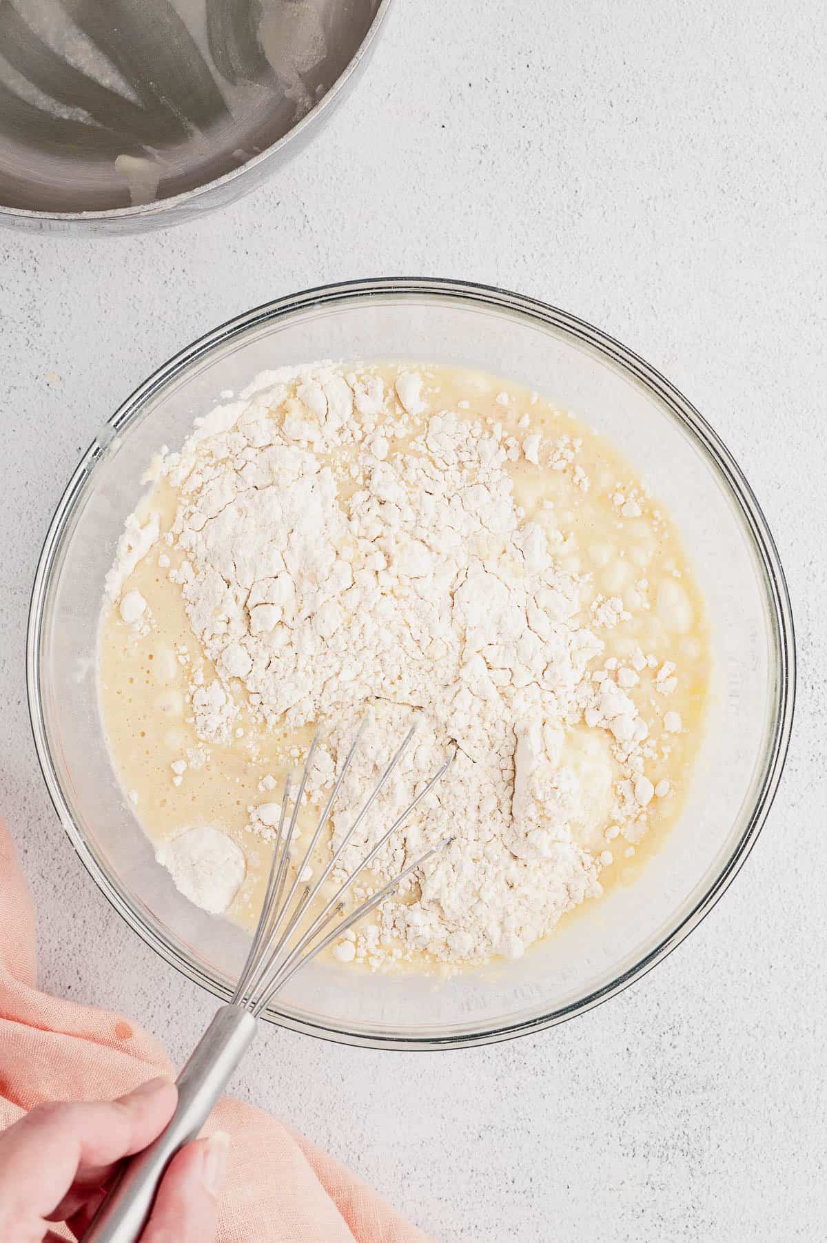 Flour is added into a bowl of cinnamon roll batter.