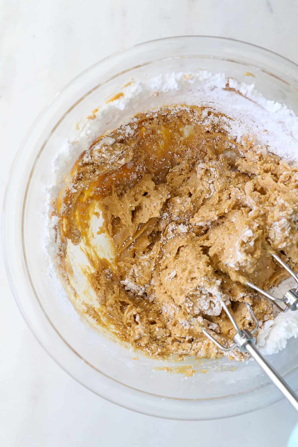An electric mixer combines the peanut butter mixture in a bowl.