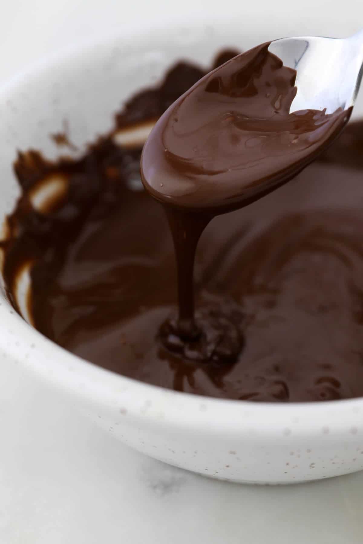 Melted chocolate drips from a spoon into a bowl of melted dark chocolate.