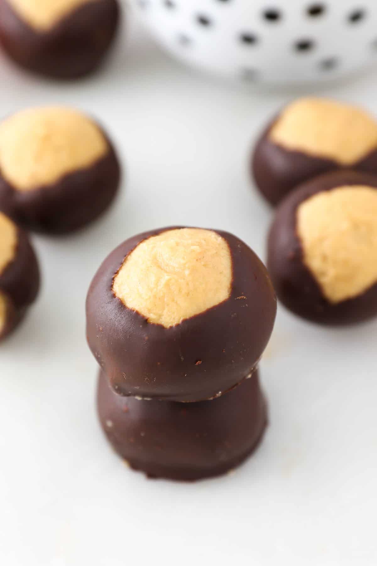 Two peanut butter buckeyes stacked on top of one another, with assorted buckeyes in the background.